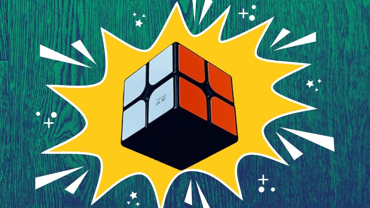 A 2x2 Rubik's Cube on a yellow starburst over a green wooden background