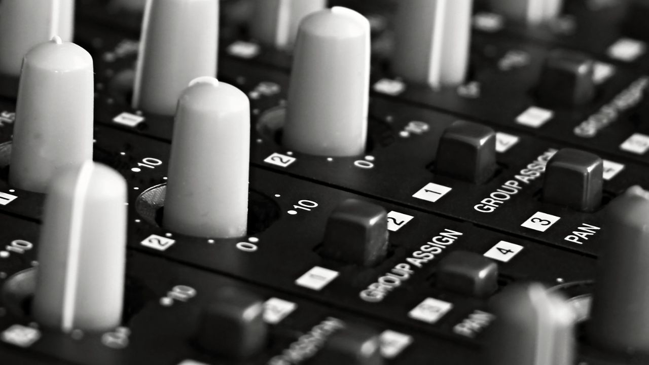 Black and white close-up of faders and group assign buttons on a mixing console