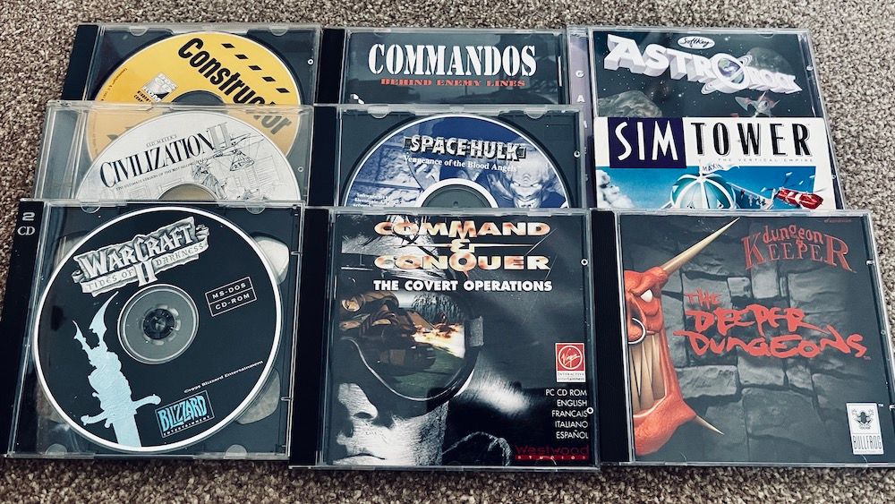 Old PC game CDs including Warcraft II, Command & Conquer, SimTower and Dungeon Keeper laid out on a carpet